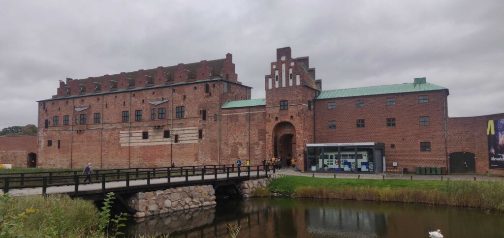 Malmöhus i gråväder. Små knektar vaktar porten långt borta, bortom bron över vallgraven.